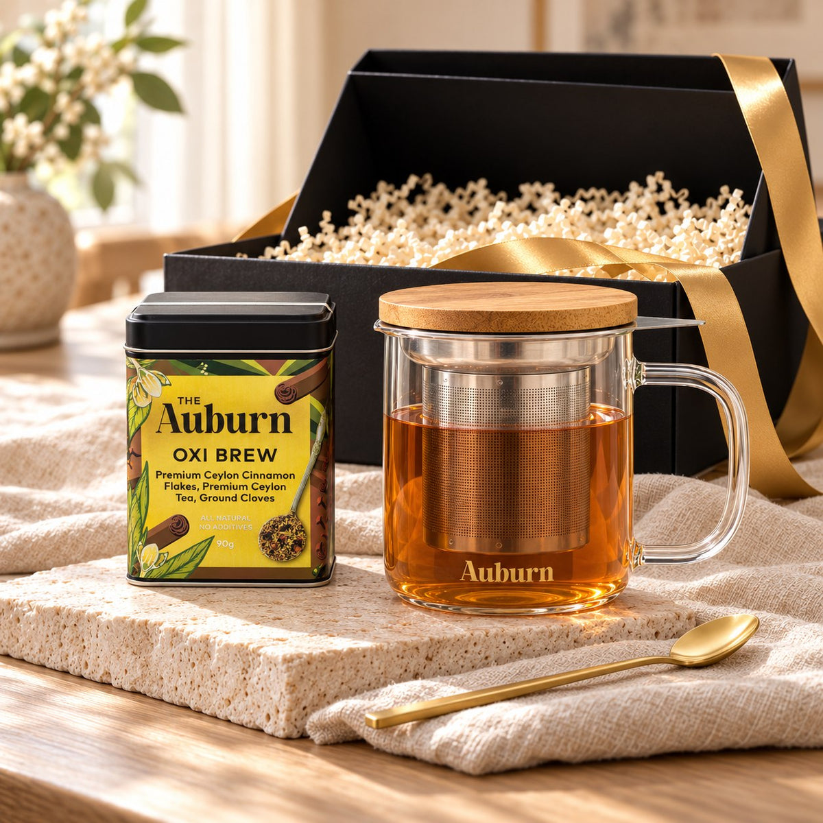 First Brew hamper: an Oxi Brew tin, a glass brewing mug with steel strainer and bamboo lid, and a gold tea spoon.