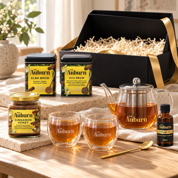 A Lovely Gift hamper: Alba and Ayu Brew tins, a glass teapot, two glass mugs, a jar of cinnamon honey, a bottle of diffuser oil and a gold tea spoon.