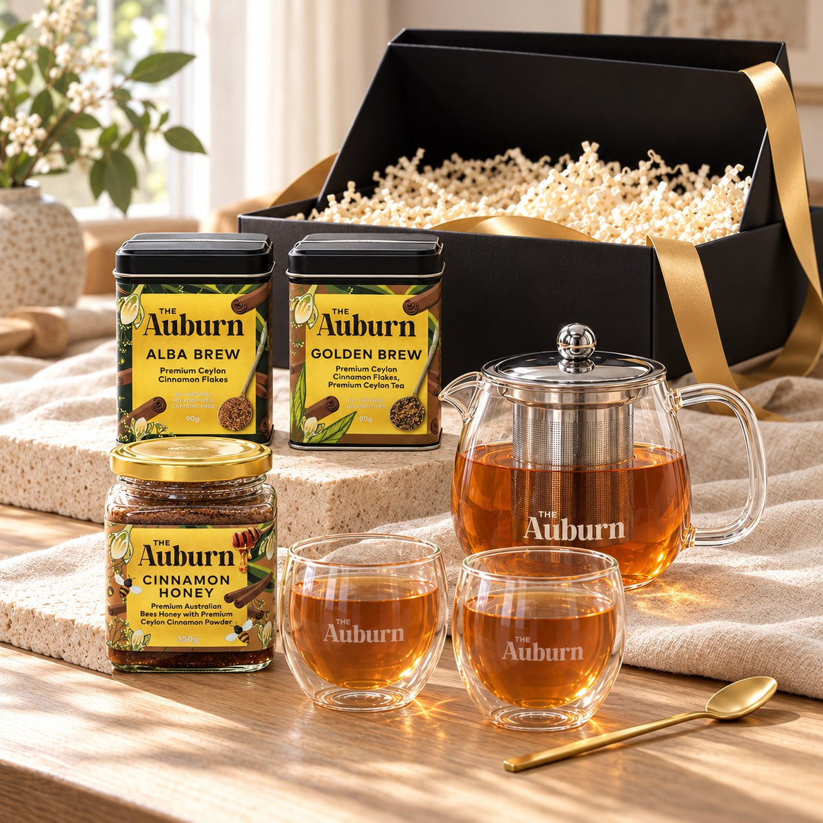 The Shared Table hamper: Alba and Golden Brew tins, a glass teapot, two glass mugs, a jar of cinnamon honey and a gold tea spoon.