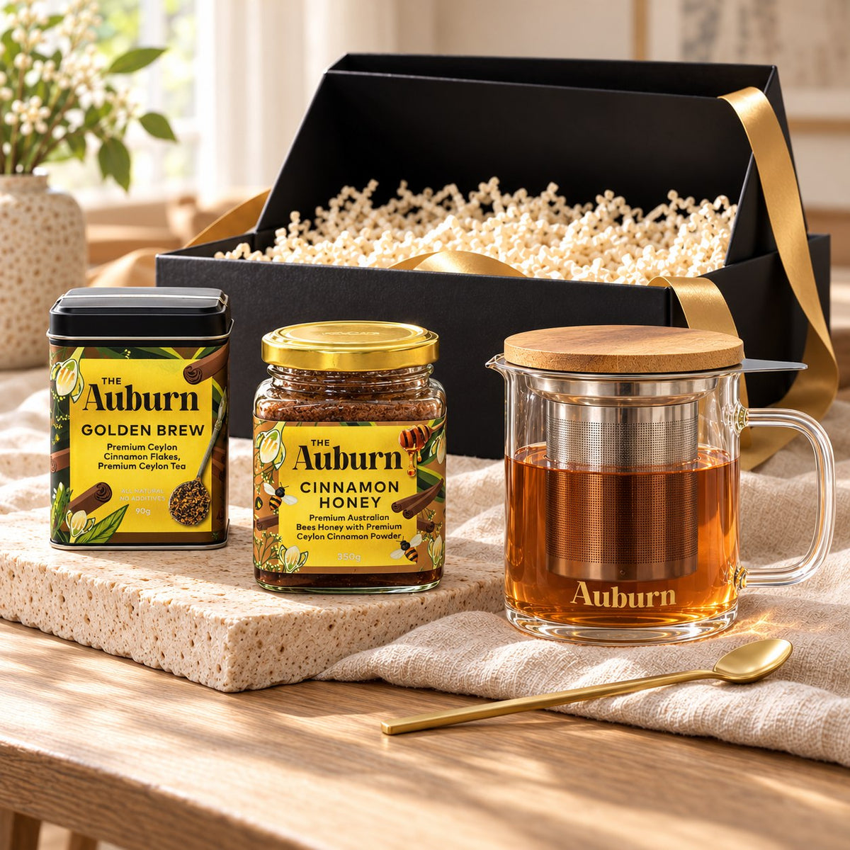 Celebrate your way hamper: a Golden Brew tin, a jar of cinnamon honey, a glass brewing mug with strainer and a gold tea spoon.