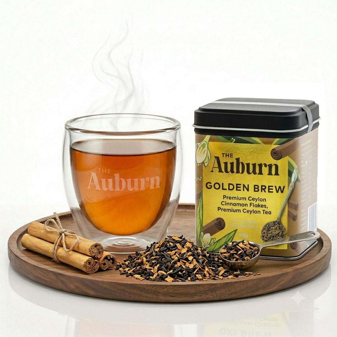 Golden Brew 90g tin beside a glass cup of brewed tea, cinnamon quills and loose tea on a wooden board